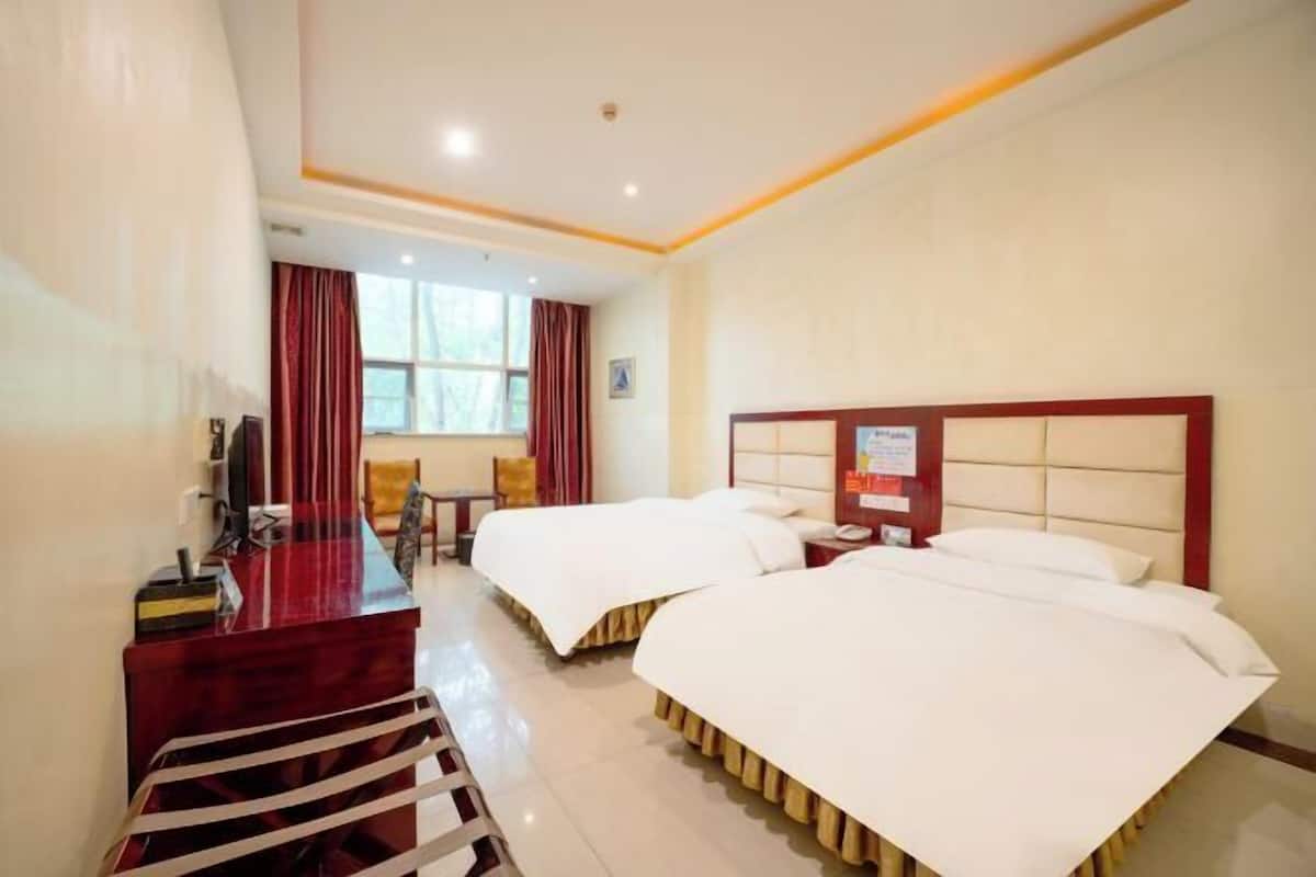 A hotel room with two beds, a desk with a chair, a TV, and a window with curtains.