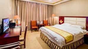 A hotel room with a bed, a desk with a computer, two chairs, and a television.
