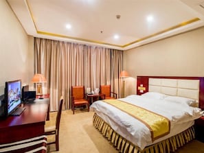 Habitación de hotel con cama, escritorio con computadora, dos sillas y televisor.