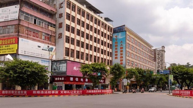 A multi-story building with commercial signage on the ground floor, surrounded by trees and a clear sky.