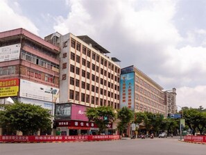 A multi-story building with commercial signage on the ground floor, surrounded by trees and a clear sky. - Huifeng Hotel (Shaoguan)