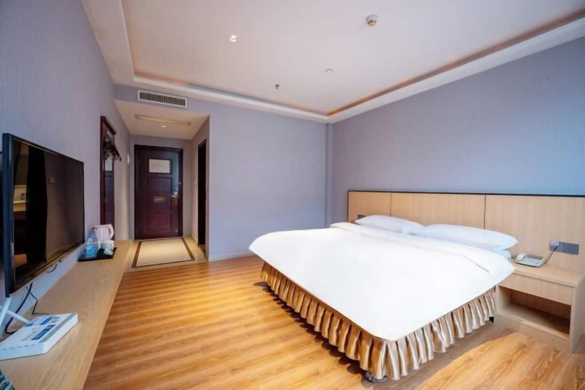 A hotel room with a large bed, a TV, a desk, and a door.