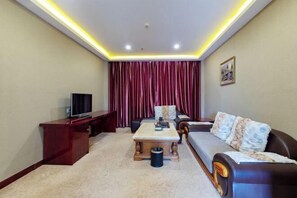 A living room with a sofa, a coffee table, a TV, and a red curtain. - Huifeng Hotel (Shaoguan)