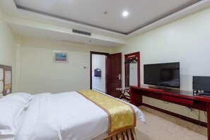 A hotel room with a bed, a desk with a TV, and a door leading to another room. - Huifeng Hotel (Shaoguan)