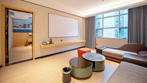 A modern hotel room with a large window, a seating area with a sofa and a round table, a flat-screen TV mounted on the wall, and a small trash bin. - Huifeng Hotel (Lechang)