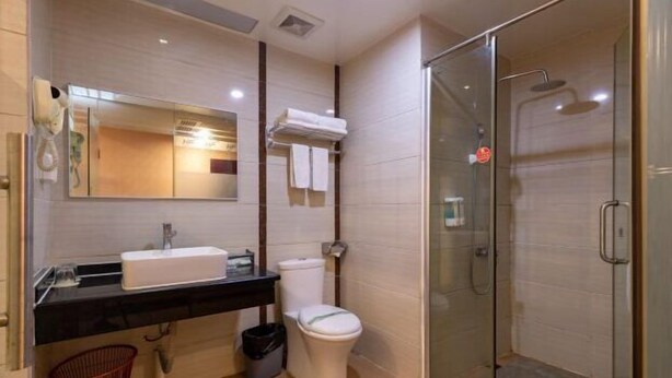 A modern bathroom with a glass-enclosed shower, a sink with a mirror, and a toilet. - Huifeng Hotel (Shaoguan)