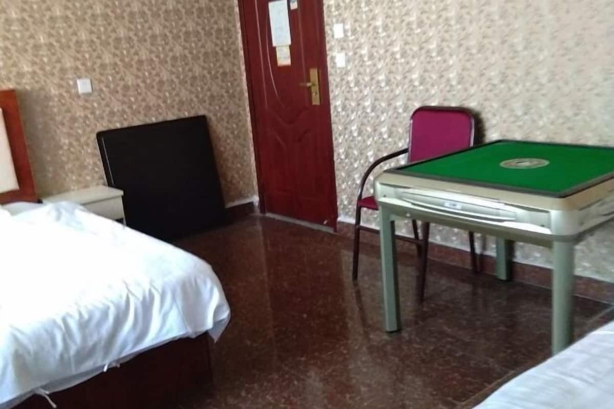 Um quarto com uma cama, uma escrivaninha com tampo verde e uma porta.
