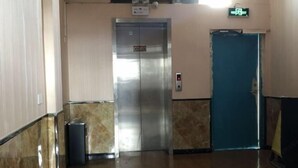 An elevator in a hallway with a marble floor and walls, a trash bin, and a blue door. - Guzhen Zihao Hotel (Guzhen)
