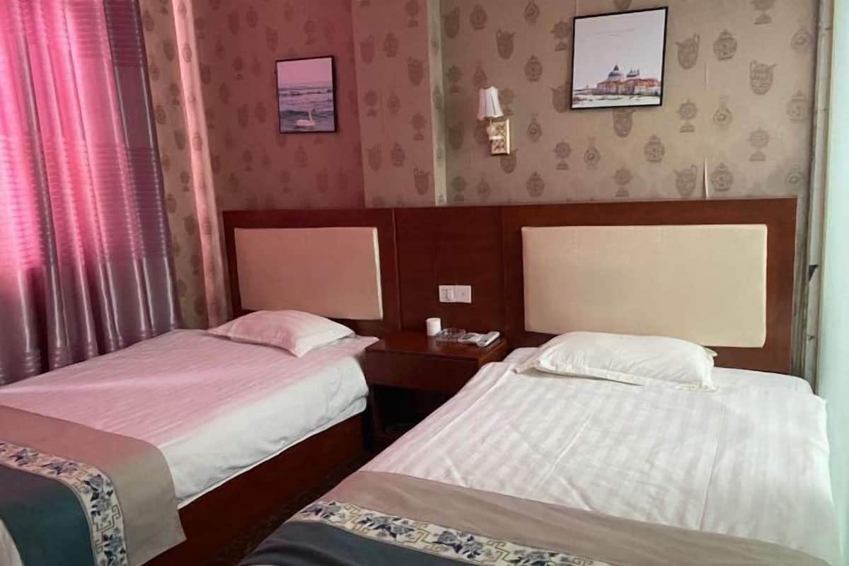 Quarto de hotel com duas camas, uma mesinha de cabeceira, uma luminária na parede e duas imagens emolduradas.