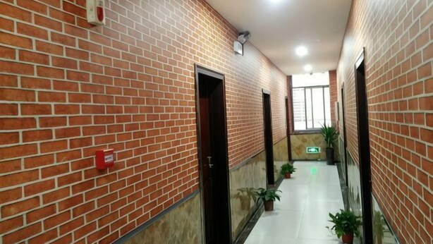 A corridor with brick walls, doors, potted plants, and a tiled floor. - Guzhen Zihao Hotel (Guzhen)