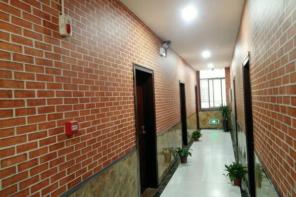 A corridor with brick walls, doors, potted plants, and a tiled floor.