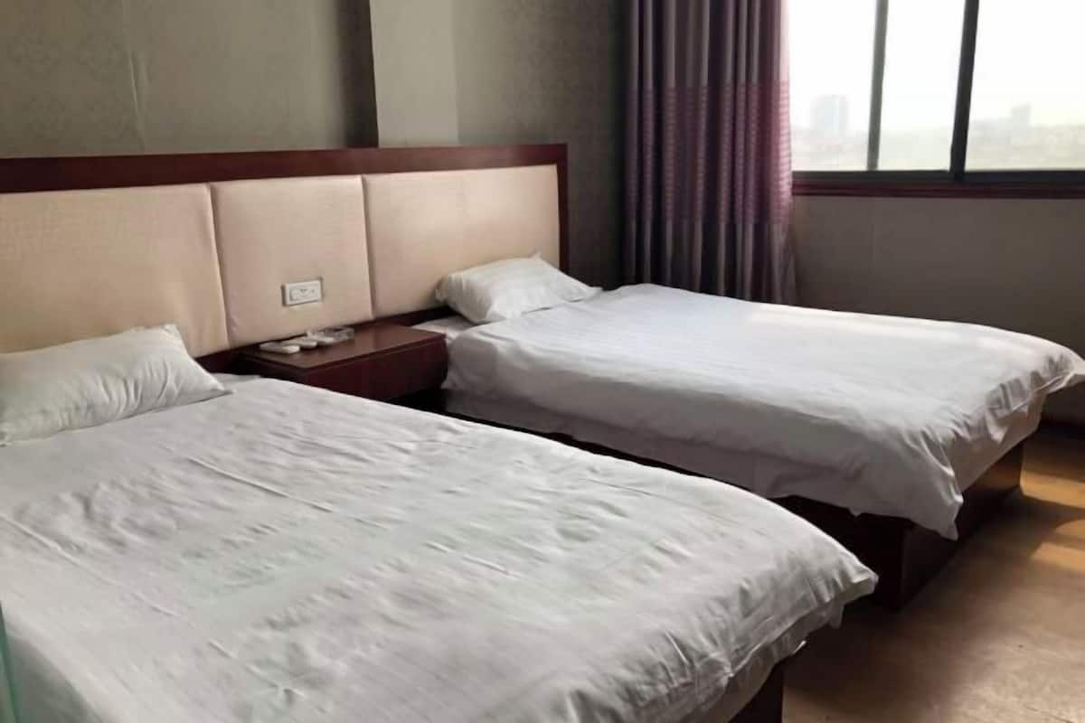 Quarto de hotel com duas camas, uma mesa de cabeceira e uma janela com cortinas.