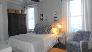 A bedroom with a bed, a nightstand with a lamp, a chair, a wardrobe, and framed pictures on the wall. - Downtown Victorian Flat Great Location and free Parking (Chattanooga)