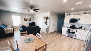 Cocina moderna con armarios blancos, microondas y estufa. Hay un comedor con mesa y sillas de madera.