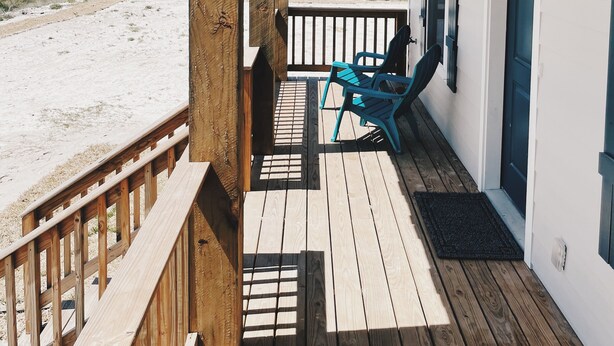 Un espacio exterior techado con una terraza de madera, una silla azul y una puerta que da a una habitación.