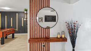 A modern living room with a foosball table, a wooden accent wall, a mounted TV, and a vase with dried flowers. - Spacious 4BR Family Home, 6 Beds, Arcade, Game Room + Park Across Street (Watauga)