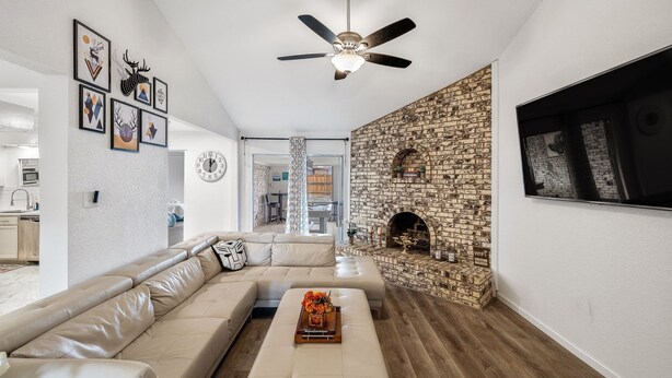 A modern living room with a stone fireplace, a ceiling fan, and a large TV mounted on the wall. - Spacious 4BR Family Home, 6 Beds, Arcade, Game Room + Park Across Street (Watauga)
