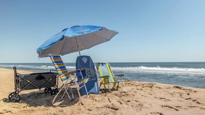 A beach scene with a blue umbrella, a beach chair, and a folding chair. - Walk to the Beach! Firepit, Fully Fenced Yard, Grill, Bikes, N64, Pets/EV! (Ocean City)