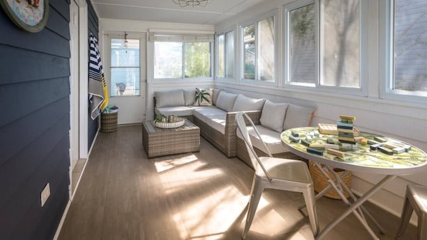 A sunlit room with a large window, a sofa, a dining table, and a small side table. - Walk to the Beach! Firepit, Fully Fenced Yard, Grill, Bikes, N64, Pets/EV! (Ocean City)