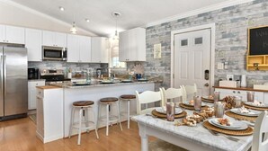 A modern kitchen with white cabinets, stainless steel appliances, and a central island with bar stools. - Walk to the Beach! Firepit, Fully Fenced Yard, Grill, Bikes, N64, Pets/EV! (Ocean City)