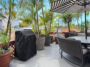 A patio with outdoor furniture, potted plants, and a striped umbrella. - Miguel's Mirador: Ocean-View Studio, Hammock Terrace, Heated Pool, Walkable (Puerto Vallarta)