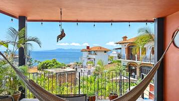 Un hamac sur un balcon donnant sur une vue côtière, avec des bâtiments et de la végétation.