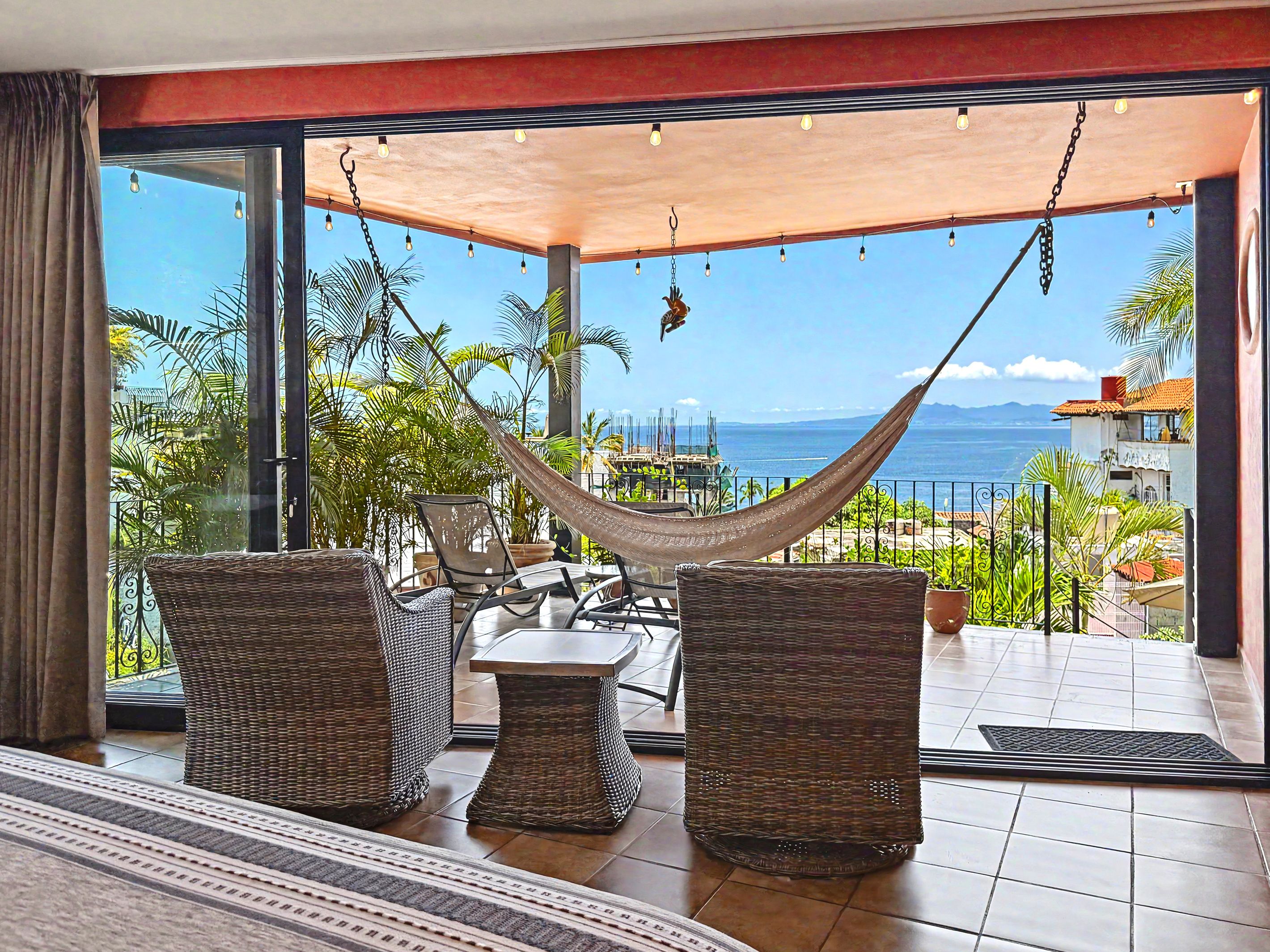 A balcony with wicker furniture, a hammock, and a view of the sea.