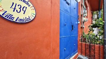 Une porte bleue avec un portail en métal, une enseigne jaune portant l’inscription « Bienvenidos 439 Villa Amistad » sur un mur rouge, et une petite marche menant à la porte.