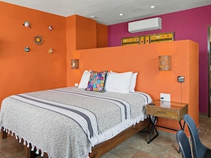 A bedroom with a bed, bedside table, chair, and decorative wall art. - Miguel's Mirador: Ocean-View Studio, Hammock Terrace, Heated Pool, Walkable (Puerto Vallarta)