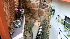 Una escalera con barandilla de metal, un muro de piedra con un espejo decorativo y plantas en macetas.