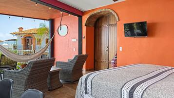 A bedroom with a bed, a hammock, wicker furniture, a television, and a large arched door.