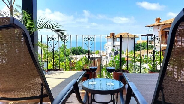 Un balcón con vista al mar, amueblado con dos sillas y una mesa, y plantas en macetas.
