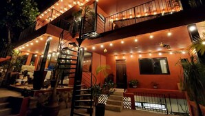 Un edificio de varios pisos con una escalera en espiral, zona de estar al aire libre y luces colgantes.