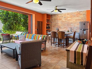 A dining area with a brick wall, a kitchen with a refrigerator, and a seating area with a colorful sofa and chairs.