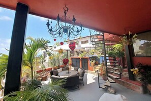 En udendørs patio med en rund siddeplads, en lysekrone og flere krukkeplanter.