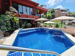 Una piscina con borde de azulejos, rodeada de plantas en macetas y mobiliario de exterior.