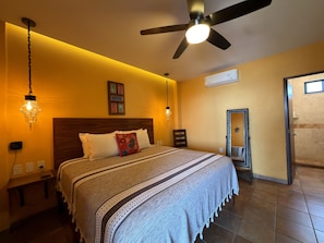 A bedroom with a bed, bedside tables, a ceiling fan, and a wall-mounted air conditioner.