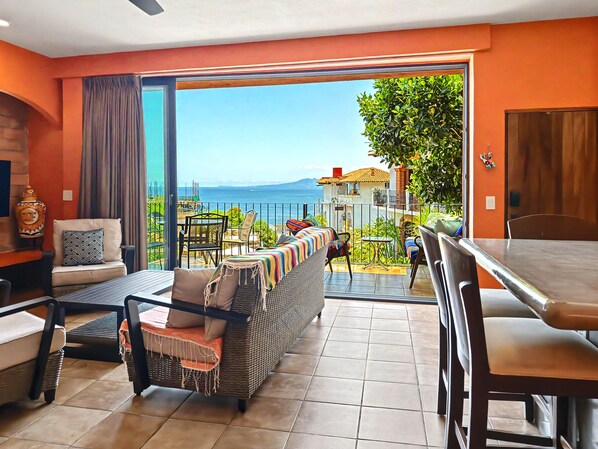 A modern living room with a large sliding glass door leading to a balcony with a view of the sea.