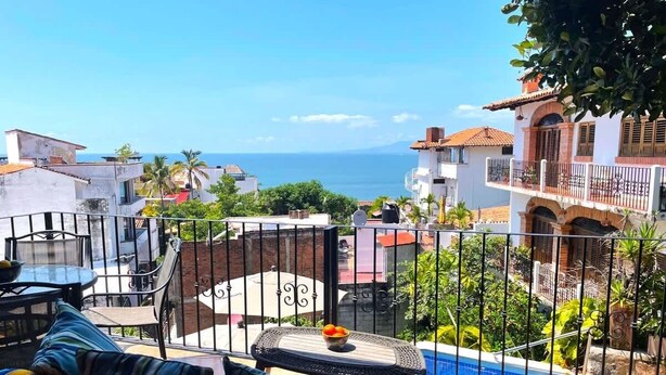A balcony with a pool, outdoor furniture, and a view of the sea. - Ivan's Bella Vista: Top-Floor 2BR, Bay Views, Heated Pool, Walkable (Puerto Vallarta)