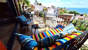 A balcony with a colorful striped sofa, a small round table, and a chair. - Ivan's Bella Vista: Top-Floor 2BR, Bay Views, Heated Pool, Walkable (Puerto Vallarta)