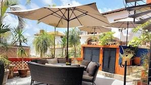 An outdoor patio with wicker furniture, a large umbrella, and potted plants.