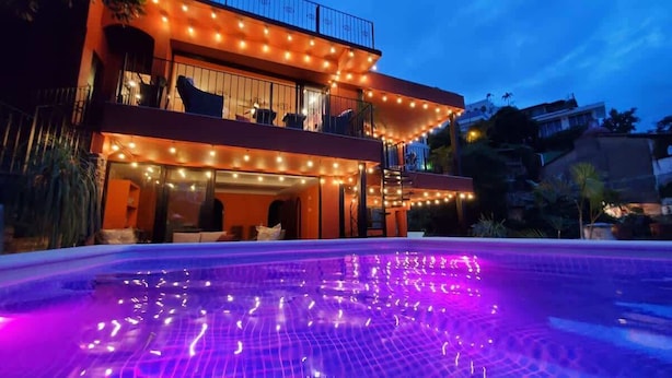 A two-story building with a swimming pool at the front, featuring string lights and a water feature.