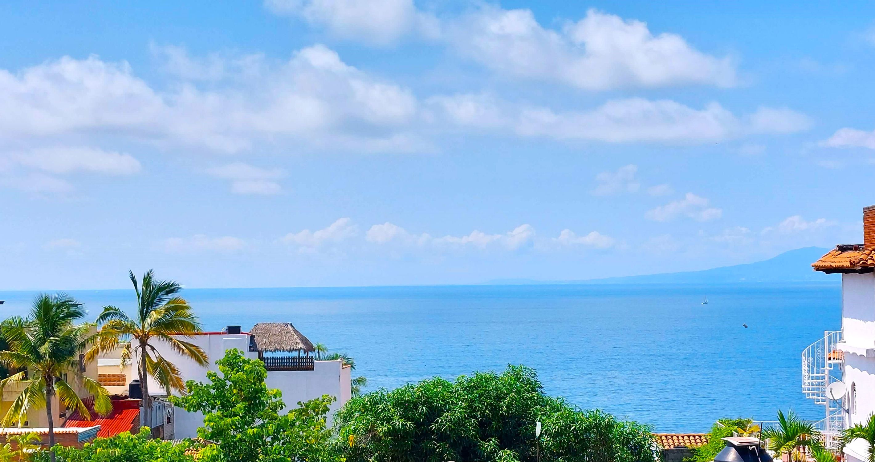 Vista costera con cielo despejado, mar tranquilo y edificios de estilo arquitectónico tradicional.