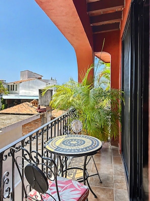 A balcony with a tiled floor, a round table with a patterned tablecloth, and a chair.