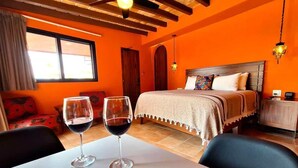 A room with a bed, two wine glasses on a table, and a window.