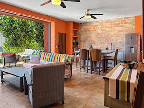 A dining area with a brick wall, a kitchen with a refrigerator, and a seating area with a colorful sofa and chairs.