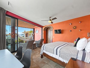 Ein Schlafzimmer mit Bett, Fernseher, Deckenventilator, Hängematte und einem Balkon mit Stühlen.