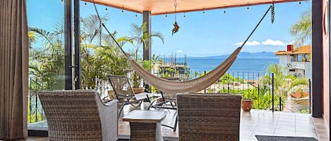 A balcony with wicker furniture, a hammock, and a view of the sea.