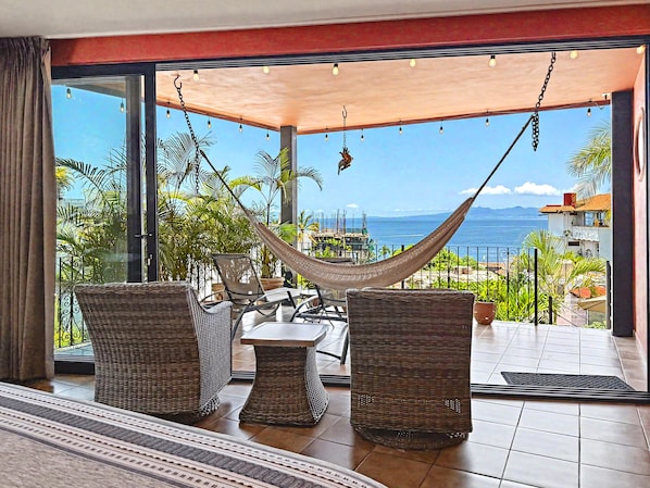 A balcony with wicker furniture, a hammock, and a view of the sea.
