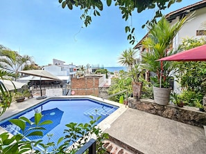 Una piscina en la azotea con vistas al mar, rodeada de vegetación y edificios.